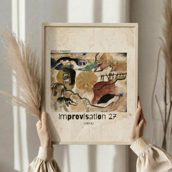 May include: Hands holding a framed abstract art print showing swirling organic forms in earthy tones of brown, green, yellow and blue against a cream background. The artwork features flowing, biomorphic shapes that suggest movement and energy. The print is displayed in a light wooden frame with cream matting, held against soft beige curtains with dried pampas grass visible to the left side.