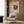 May include: Framed abstract art poster featuring burgundy geometric shapes, circles, and radiating lines on cream background, displayed above a beige upholstered armchair with geometric patterned pillow. Modern living room setting with wood paneled wall, brass floor lamp, and dark round side table with open book.