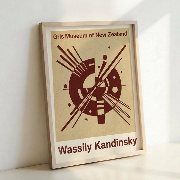 A framed abstract art print featuring bold burgundy geometric shapes on cream background. The design shows intersecting lines, circles, and angular forms in Kandinsky's distinctive style. The print is displayed in a light wood frame, leaning against a white wall with soft natural lighting creating gentle shadows.