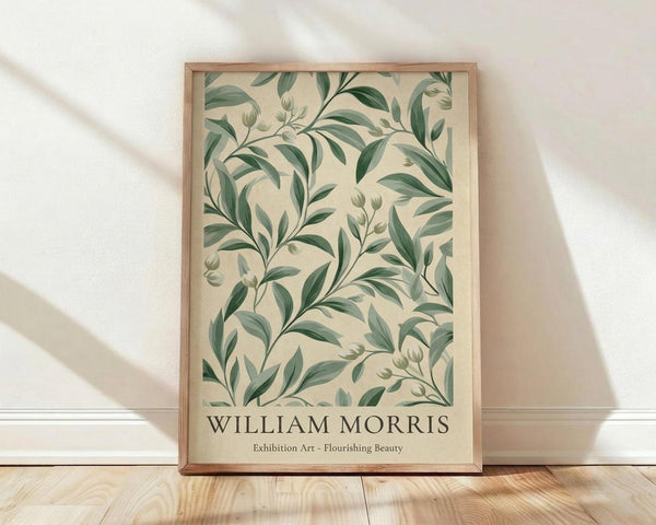 May include: Framed botanical art print leaning against white wall on light wood floor with natural shadows. Features green leaves and stems in William Morris style on cream background with thin wood frame. Exhibition-style poster with text at bottom.