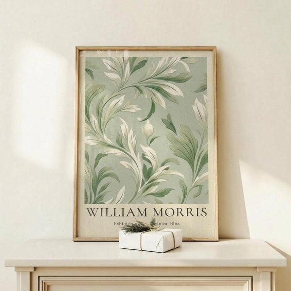 May include: Framed botanical poster with sage green background featuring flowing white and green leaf patterns in William Morris style, displayed on light wood console table beside small wrapped gift with twine and evergreen sprig against cream wall