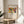 May include: Framed art print featuring Wassily Kandinsky's abstract artwork with vibrant red, yellow, blue, and green shapes depicting stylized figures in motion. The poster shows museum exhibition text reading "Klänge" and "The Art Institute of Chicago (1913)". Light wood frame sits on round wooden side table next to beige upholstered chair, with plant leaves visible on left side in bright, naturally lit room with white walls.