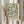 May include: Hands holding a framed botanical art print featuring green leafy branches with small buds on a cream background, displayed against white curtains with dried pampas grass visible to the left, person wearing a beige ruffled sleeve top