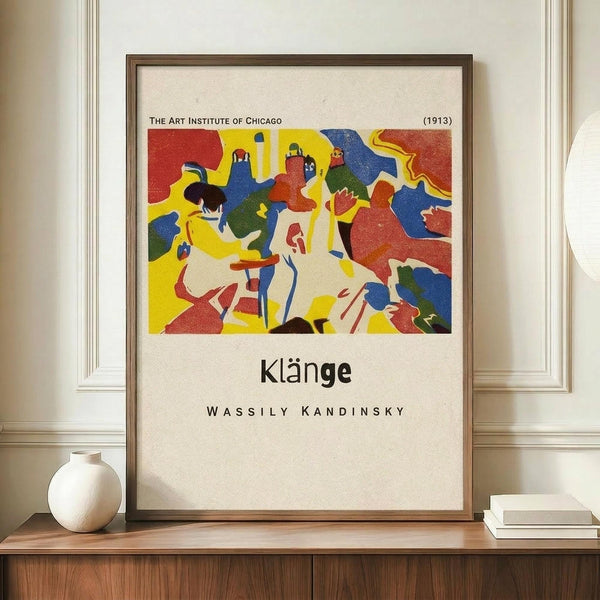 May include: Framed art print featuring Wassily Kandinsky's abstract expressionist artwork with bold red, yellow, blue and green shapes depicting stylized figures in motion. The poster shows "The Art Institute of Chicago (1913)" at top and "Klänge" and "Wassily Kandinsky" text below the colorful artwork. Wooden frame sits on mid-century modern walnut credenza alongside white ceramic vase and stacked books against cream wainscoting wall.