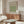 May include: Framed William Morris botanical pattern poster in sage green displayed above walnut credenza in minimalist room with cream chair, glass coffee table, and modern lamp. Natural sunlight creates warm shadows across neutral walls and furnishings.