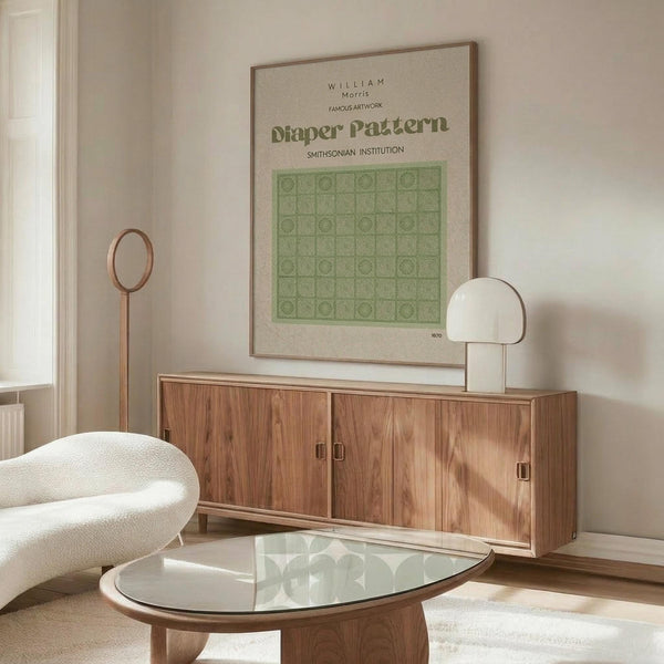 May include: Framed William Morris botanical pattern poster in sage green displayed above walnut credenza in minimalist room with cream chair, glass coffee table, and modern lamp. Natural sunlight creates warm shadows across neutral walls and furnishings.