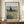 May include: Framed Van Gogh reproduction poster showing a golden wheat field with tall dark cypress tree and cloudy sky, displayed on wooden sideboard next to white ceramic vase and stacked books in room with cream walls and white trim molding.