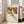 May include: Framed art print leaning against white wall next to beige upholstered armchair in bright living room. Print features colorful abstract artwork with bold red, yellow, blue, and green shapes depicting stylized figures. Museum-style poster format with cream matting, thin light wood frame. Natural sunlight streaming through tall windows creates soft shadows on hardwood floor.