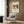 May include: Framed art poster with colorful abstract design featuring bold red, blue, and yellow shapes displayed on wood paneled wall above beige upholstered armchair with geometric patterned pillow. Modern brass floor lamp and dark round side table with open book visible in contemporary neutral-toned room setting.