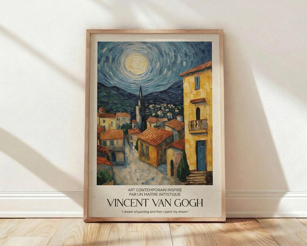 May include: Framed poster print featuring a Mediterranean village scene in Van Gogh's distinctive swirling style, with warm yellow and orange buildings topped with terracotta roofs beneath a dramatic blue night sky with circular, spiraling clouds around a bright moon. The artwork shows cobblestone streets winding between rustic houses and a tall minaret or tower. Natural wood frame with cream matting displays the poster against white walls on light wooden flooring with soft natural lighting.