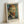 May include: Framed poster print of a self-portrait showing a man with reddish-brown hair and beard, blue eyes, wearing a dark jacket with white collar. The artwork features swirling brushstrokes in blues and greens typical of post-impressionist style. Natural wood frame with white matting displays the print, which includes "Vincent van Gogh" and "self portrait" text below the image. Frame leans against white wall on light surface.