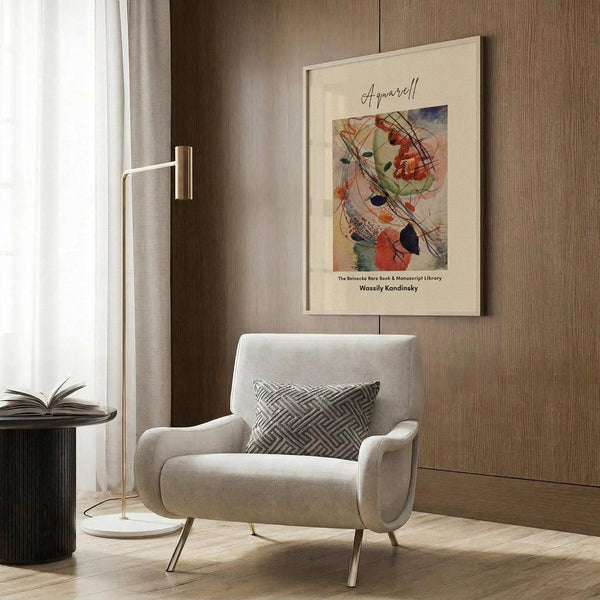 May include: Framed abstract art print hanging on wood paneled wall above modern cream armchair with geometric pillow. Colorful watercolor artwork features swirling lines, circles and organic shapes in red, orange, green and blue tones. Contemporary room setting with brass floor lamp, dark side table with open book, and natural lighting from window with curtains.
