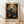 May include: Framed poster print in light wood frame leaning against white wall on wooden floor. Features ornate botanical design with blue bird perched among flowering vines, orange and coral blooms, and decorative scrollwork in William Morris style. Rich teal, coral, and cream colors with vintage aesthetic. Text below reads "WILLIAM MORRIS Exhibition Art - Colorful Petals." Natural lighting creates soft shadows on textured white wall.