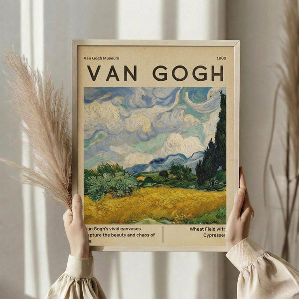 May include: Person in cream ruffled blouse holding framed Van Gogh museum poster against white curtained window. Print features swirling blue and white clouds over golden wheat field with dark cypress trees and green landscape. Dried pampas grass visible on left. Warm natural lighting creates soft shadows on beige poster with black text.