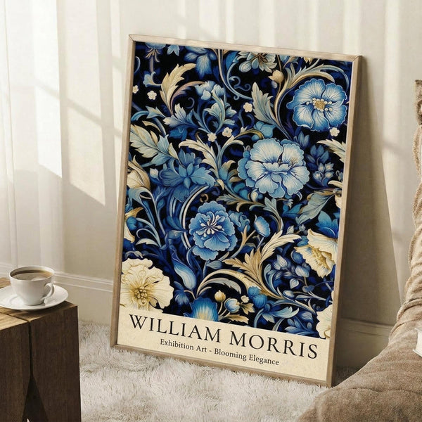 May include: Framed poster with intricate blue floral pattern featuring ornate blooms and flowing foliage on dark navy background with cream text at bottom, leaning against white wall corner next to wooden side table with white teacup and saucer, positioned on light wooden floor beside beige textured throw blanket