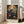 May include: Framed poster featuring a blue bird perched among flowering branches with coral peonies and cream blooms against a dark teal background, displayed in a bright living room with white walls, large windows, and a beige sectional sofa on light wooden floors.