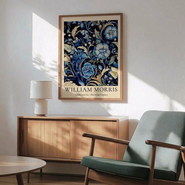 May include: Framed botanical poster with intricate blue and cream floral pattern on dark background, displayed above wooden sideboard with white ceramic lamp. Mid-century modern sage green armchair with wooden arms sits nearby on light wooden floors. Natural sunlight creates geometric shadows on white wall, creating warm, contemporary living room setting.