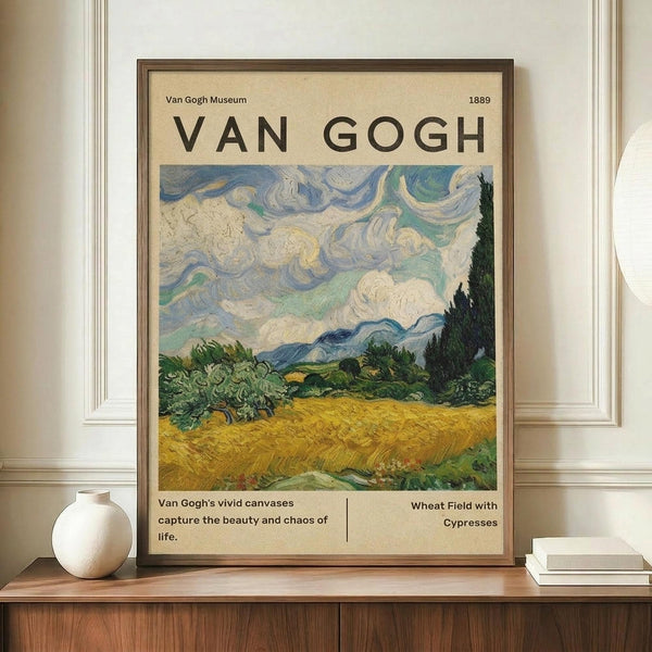 May include: Van Gogh museum poster featuring Wheat Field with Cypresses painting in brown frame, displayed on wooden credenza beside white ceramic vase and stacked books. Poster shows swirling blue-green sky above golden wheat field with dark cypress trees. Cream background with black text including museum attribution and painting title.