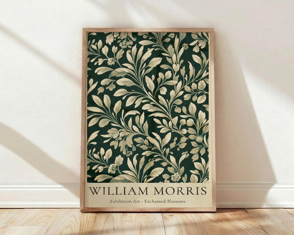 May include: Framed poster with dark green background featuring cream-colored botanical pattern of flowing leaves, branches and small flowers in William Morris style. Natural wood frame leans against white wall on light wooden floor with soft window light creating shadows across the scene.
