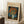 May include: Framed vintage-style art print featuring Van Gogh's vibrant orange poppies in a pale green vase against deep blue background, leaning against white wall corner near wooden side table with white coffee cup, positioned on white textured rug next to beige fabric