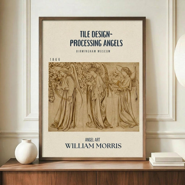 May include: Framed vintage-style poster featuring sepia-toned illustration of four angels in flowing robes with wings and halos, displayed on wooden credenza beside white ceramic vase and stacked books against cream paneled wall. The artwork shows classical Pre-Raphaelite styling with museum exhibition text layout in dark typography on cream background within thin dark wooden frame.