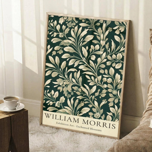 May include: Framed poster with dark green background featuring intricate cream-colored botanical pattern of flowing leaves, branches and small flowers in William Morris style, displayed leaning against white wall corner next to wooden side table with white coffee cup and beige knit throw blanket on textured rug.