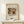 May include: Framed art print featuring an abstract painting with flowing organic forms in earthy tones of brown, green, yellow and black, displayed on a light wood shelf against a cream textured wall. A small wrapped gift box with twine and greenery sits beside the wooden frame.