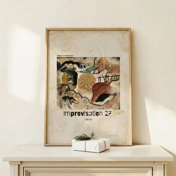May include: Framed art print featuring an abstract painting with flowing organic forms in earthy tones of brown, green, yellow and black, displayed on a light wood shelf against a cream textured wall. A small wrapped gift box with twine and greenery sits beside the wooden frame.