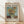 May include: Framed Van Gogh sunflower poster in light wood frame leaning against white wall on wooden floor. Print features three golden sunflowers in green ceramic vase against turquoise background. Museum-style design with "VAN GOGH" text at top, year 1888, and descriptive text below artwork. Soft natural lighting creates diagonal shadows across the scene.