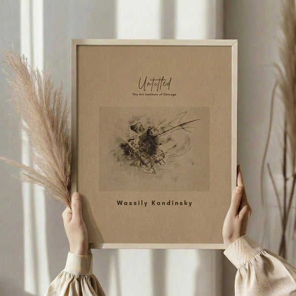 May include: Person in cream ruffled blouse holding framed abstract artwork with dark gestural marks on beige paper, standing near window with dried wheat stems, neutral toned room setting
