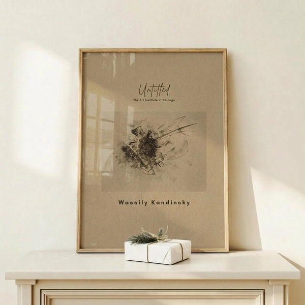 May include: Framed beige art print featuring abstract black linear drawing leaning against white wall on light wood surface. Small white wrapped gift with twine and greenery sits beside the thin wooden frame. Soft natural lighting creates gentle shadows on the minimalist display.