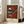 May include: Framed vintage-style museum poster featuring Wassily Kandinsky's abstract geometric artwork "Gris" with orange background, black triangular and striped shapes, and circular elements. The cream-colored poster shows "Museum of New Zealand" at top and artist name at bottom. Displayed leaning against white wall next to beige upholstered chair in bright, naturally-lit room with large windows and light wood floors.