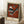 May include: Framed abstract art poster with rust-orange background featuring geometric shapes including striped triangles, circles, and angular forms in black, white, and blue tones. Text reads "Museum of New Zealand" at top and "GRIS Wassily Kandinsky" at bottom. Poster leans against white wall next to wooden block with white coffee cup and saucer, on textured cream rug with beige fabric visible.