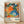 May include: A framed exhibition poster featuring vibrant abstract floral patterns in orange, blue, green, and pink with polka dots and organic shapes. The poster displays dates "28. APRIL - 14. MAI 1984" at top and "YAYOI KUSAMA" with Japanese characters at bottom, along with "MUSÉE D'ART MODERNE DE LA VILLE DE PARIS." The light wood frame sits on wooden flooring against a white wall with natural lighting creating soft shadows.