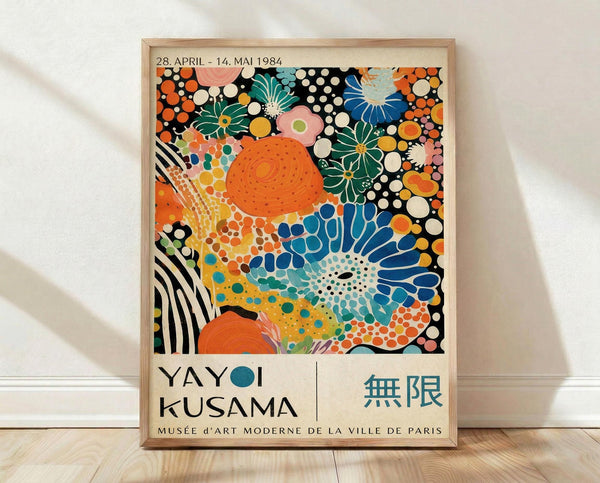 May include: A framed exhibition poster featuring vibrant abstract floral patterns in orange, blue, green, and pink with polka dots and organic shapes. The poster displays dates "28. APRIL - 14. MAI 1984" at top and "YAYOI KUSAMA" with Japanese characters at bottom, along with "MUSÉE D'ART MODERNE DE LA VILLE DE PARIS." The light wood frame sits on wooden flooring against a white wall with natural lighting creating soft shadows.