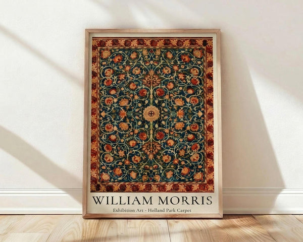 May include: Framed poster print featuring an ornate Victorian carpet design with intricate floral patterns on a dark teal background, surrounded by a decorative red and gold border. The artwork displays swirling botanical motifs with orange and rust-colored flowers throughout. Light wooden frame rests against a white wall on natural wood flooring, with soft natural lighting creating gentle shadows.