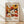 May include: Framed exhibition poster featuring colorful retro floral pattern with orange, white, and brown daisies and abstract flowers against dark background. Text shows dates April 28 - May 14, 1984 and Musée d'Art Moderne de la Ville de Paris. Light wood frame sits on wooden floor against white wall with soft shadows.