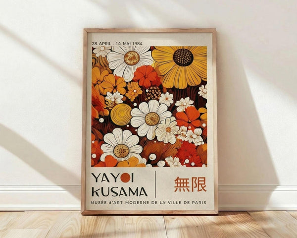 May include: Framed exhibition poster featuring colorful retro floral pattern with orange, white, and brown daisies and abstract flowers against dark background. Text shows dates April 28 - May 14, 1984 and Musée d'Art Moderne de la Ville de Paris. Light wood frame sits on wooden floor against white wall with soft shadows.