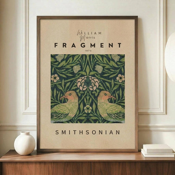 May include: Framed vintage botanical poster featuring William Morris Fragment 1876 design with symmetrical green parrots among pink flowers and foliage on cream background, displayed on wooden sideboard beside white ceramic vase and stacked books in elegant room with white paneled walls