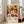 May include: Framed vintage exhibition poster featuring colorful floral pattern with white daisies, orange and yellow blooms on dark background, displayed against white wall next to beige sofa in bright living room with large windows and natural lighting.