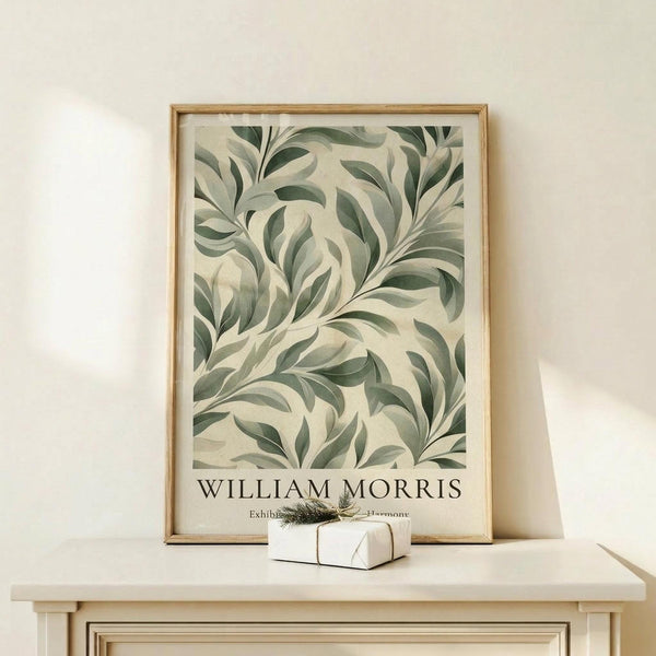 May include: Framed botanical art print with flowing green and cream leaf patterns in wooden frame, displayed on light wood console table beside small wrapped gift with natural twine and greenery sprig, against cream wall with soft natural lighting