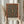 May include: Person in cream clothing holding framed botanical print featuring intricate floral carpet pattern with teal blue center, ornate red and gold border, and detailed flowers throughout. Light wood frame against neutral background with dried wheat stems visible to left side.