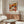 a living room with a large floral poster on the wall, a wooden cabinet, a white sofa, and a glass coffee table.