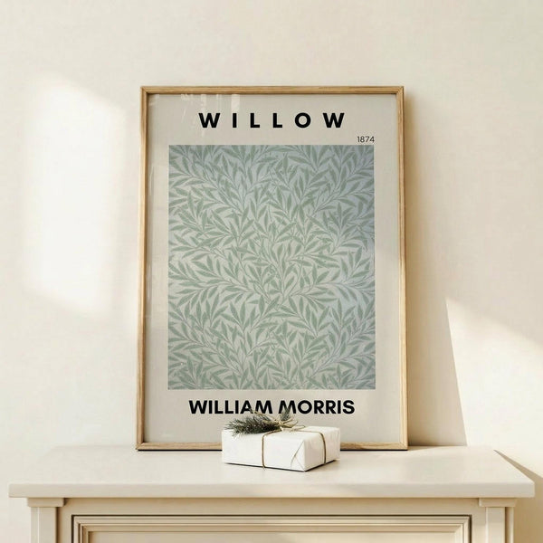 May include: Framed botanical poster with sage green willow leaf pattern on cream background, displayed on light wood console table with small wrapped gift box beside it, against neutral wall in minimalist home setting