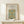 May include: Framed botanical poster with ornate blue and gold floral pattern displayed on light wood console table against cream wall. Small white wrapped gift with evergreen sprig sits in front of natural wood frame. Arts and crafts style wallpaper design features intricate vines, flowers and decorative motifs in teal, golden yellow and green tones.