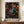 May include: A framed poster featuring Yayoi Kusama's distinctive dot art style with vibrant multicolored circles, spirals, and organic patterns against a black background, displayed on a wooden sideboard next to a white ceramic vase and books in an elegant room with cream walls and white molding.