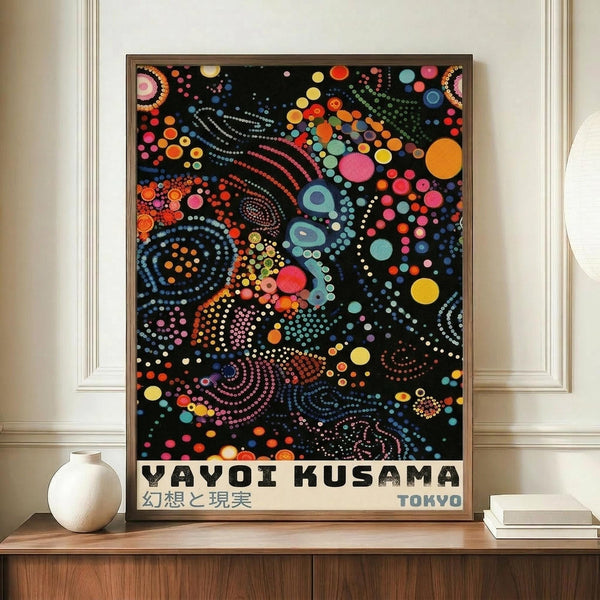 May include: A framed poster featuring Yayoi Kusama's distinctive dot art style with vibrant multicolored circles, spirals, and organic patterns against a black background, displayed on a wooden sideboard next to a white ceramic vase and books in an elegant room with cream walls and white molding.