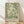 May include: Framed poster with flowing green botanical pattern featuring swirling acanthus leaves and organic flourishes on cream background, displayed in light wooden frame against white textured wall with natural sunlight shadows, positioned on light wood floor