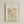 May include: Framed poster print hanging on beige wall featuring William Morris Garden Tulip pattern from 1885 Birmingham. Design shows red-orange tulips with green stems against intricate golden-brown decorative background with swirling botanical motifs. Light wood frame with white matting surrounds the vintage Arts and Crafts wallpaper design.