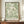 May include: A framed botanical art print featuring flowing green foliage patterns on cream background, displayed on a wooden credenza next to a white ceramic vase and stacked books. The print has William Morris text at bottom and sits against cream wainscoted walls in an elegant interior setting.